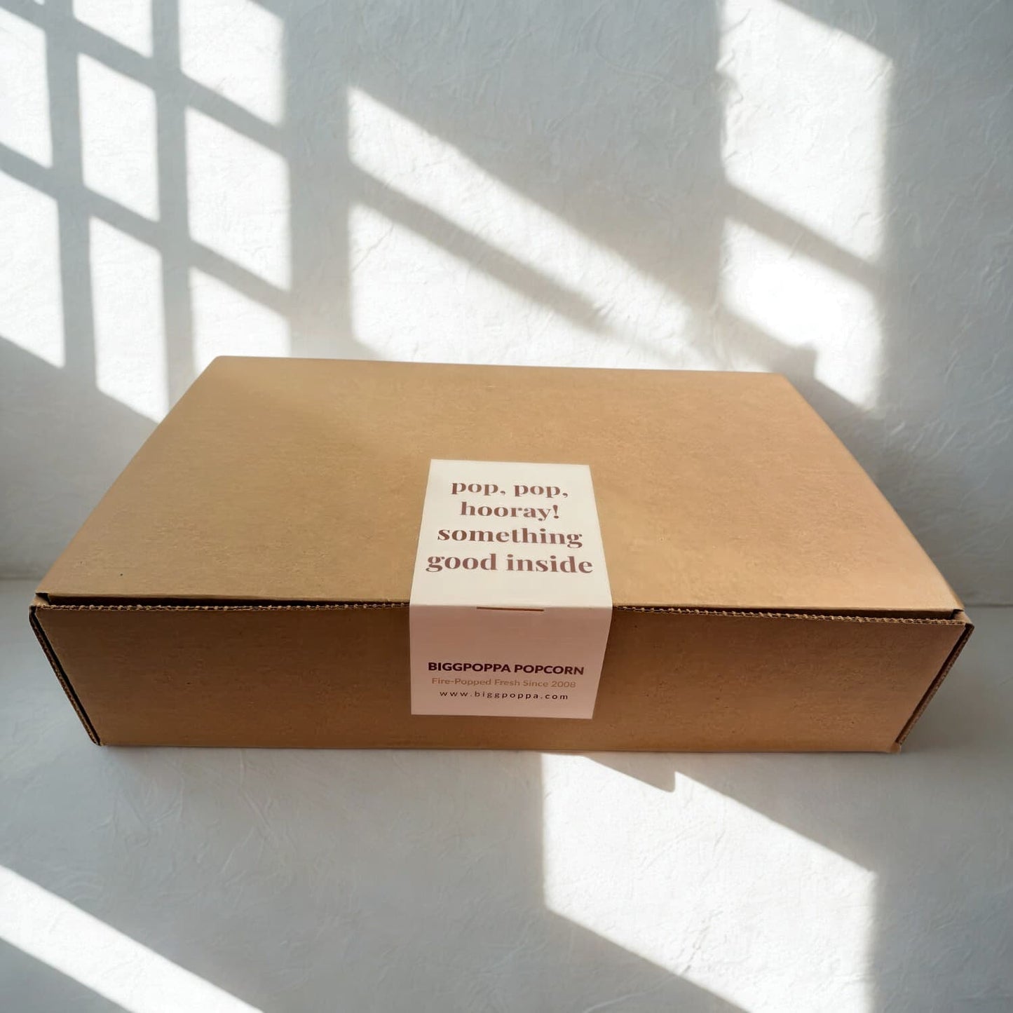 Kraft box with a white label on a light surface with shadows from window blinds.
