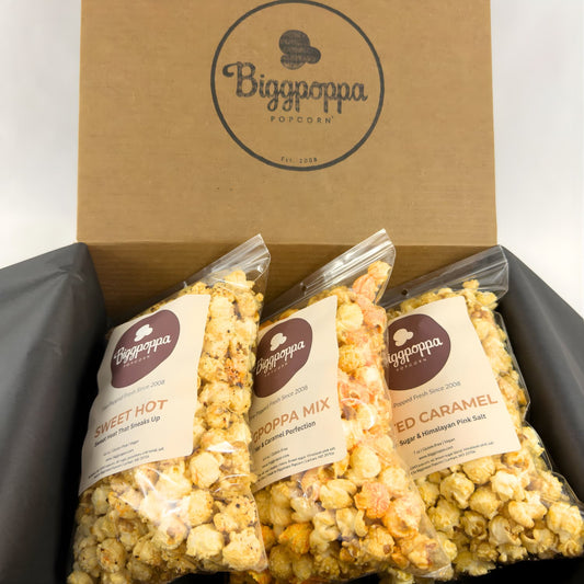 Three bags of Biggpoppa Popcorn in a rustic kraft box with three party size bags of gourmet popcorn.