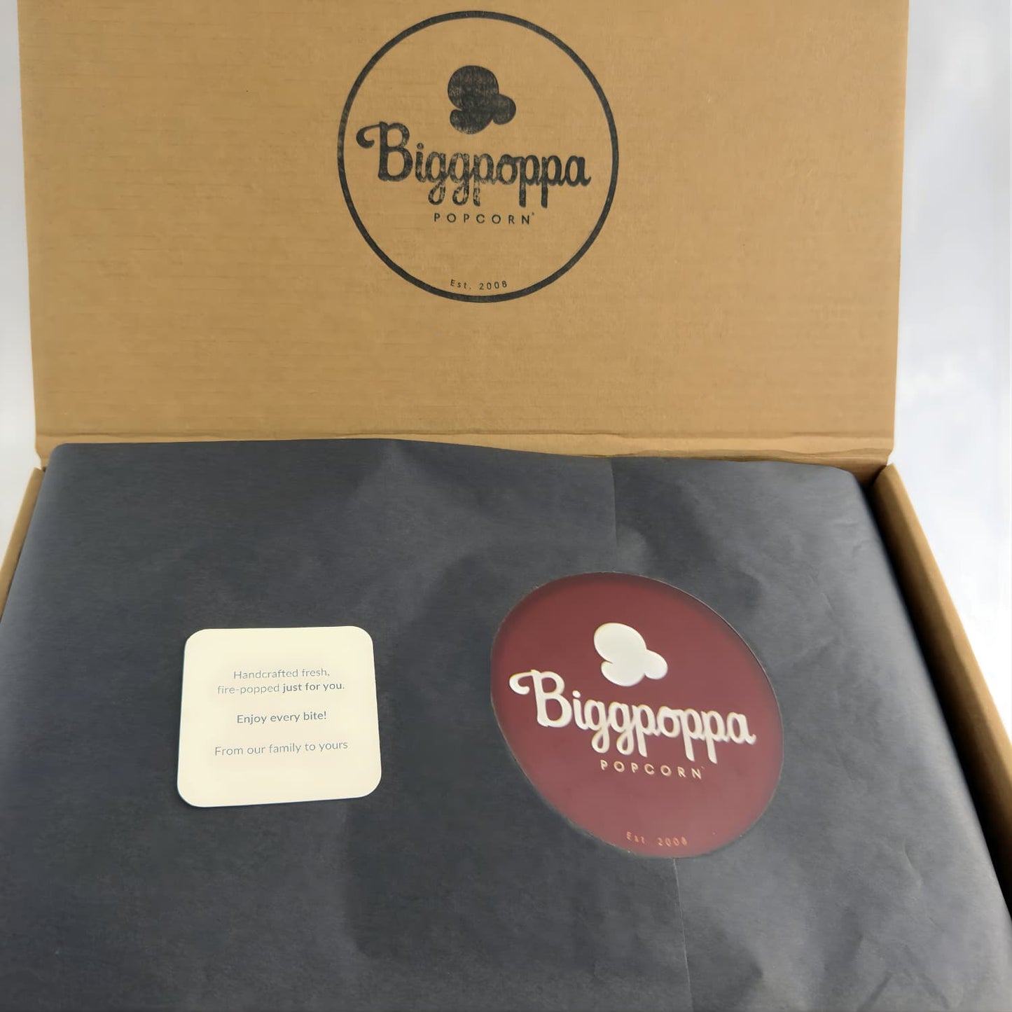 Biggpoppa Popcorn packaging with a kraft box, card, and black paper inside.