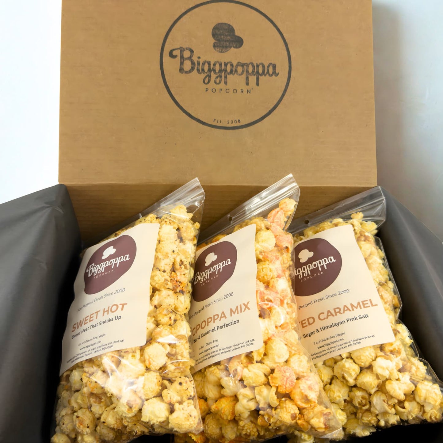 Three bags of Biggpoppa Popcorn in a rustic kraft box with visible branding.