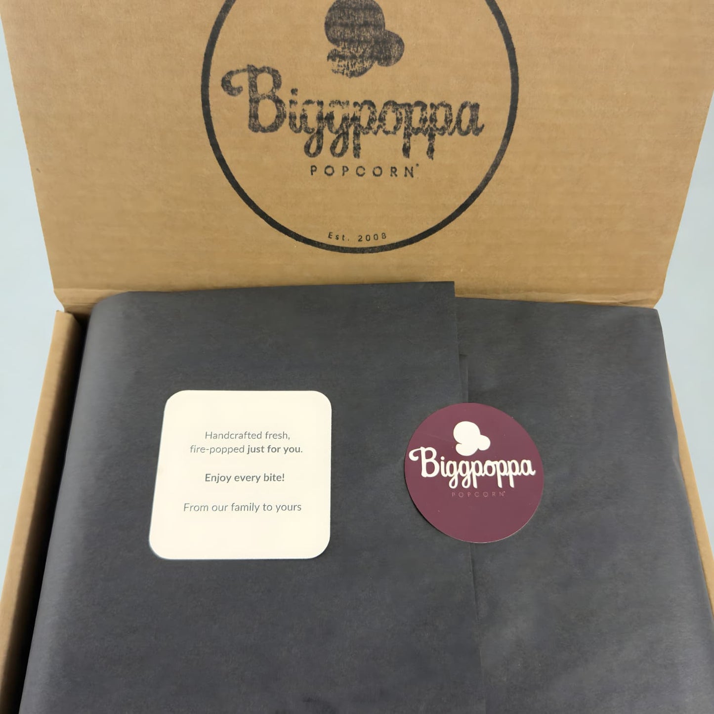 Biggoppa Popcorn Snack Pack packaging with a rustic kraft box, premium black tissue paper, and branded sticker to seal.