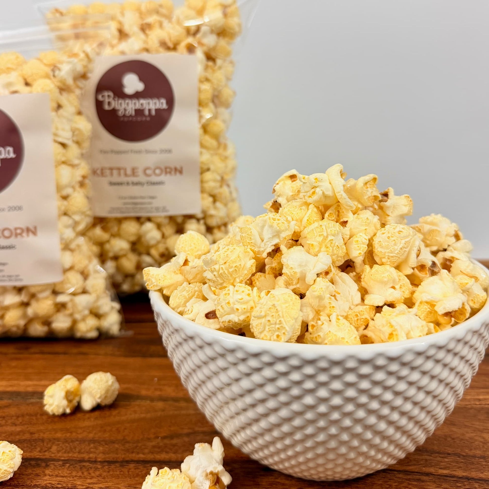 Bowl of popcorn with bags labeled Kettle Corn' on a wooden surface.