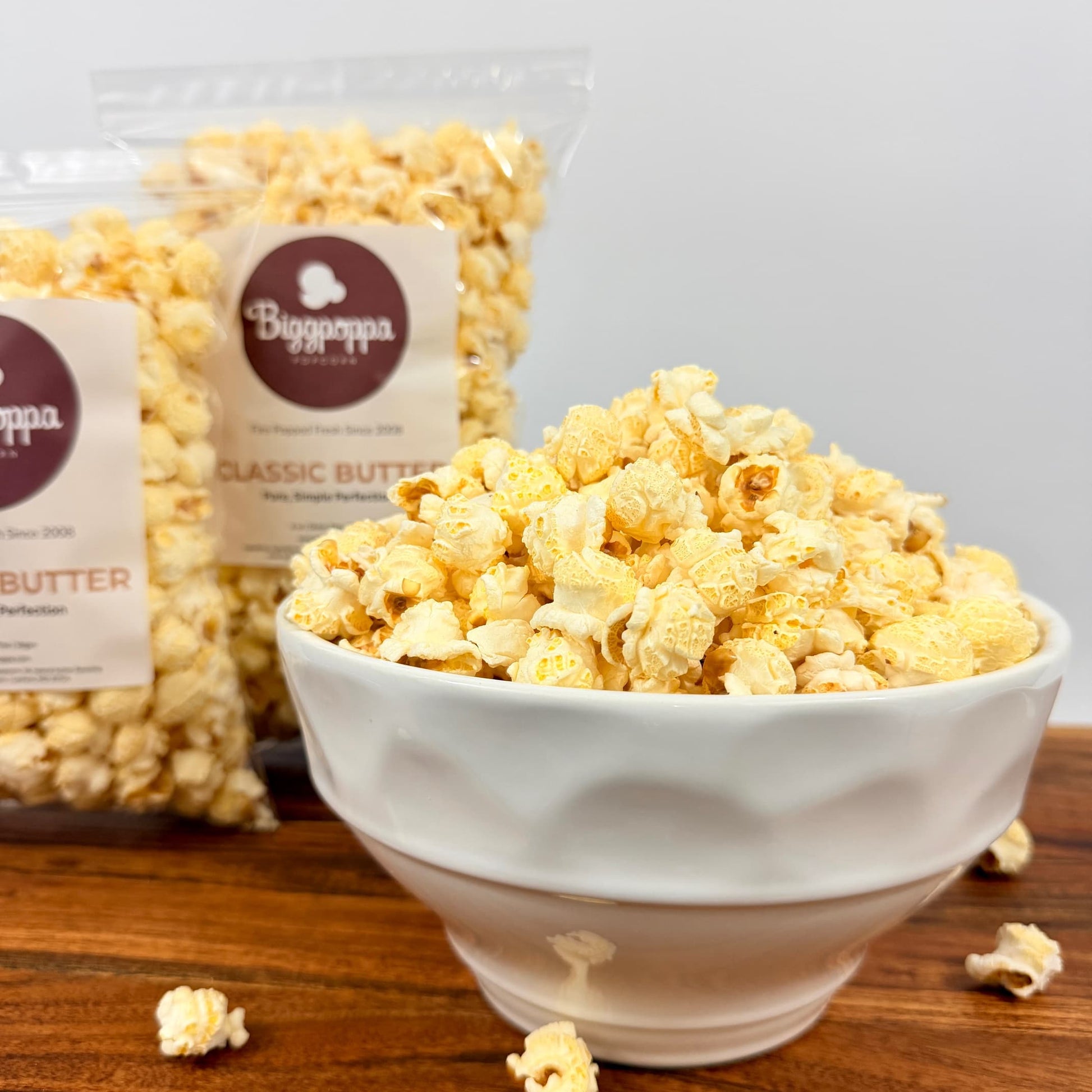 Bowl of popcorn with a bag of Biggappa's Classic Butter popcorn in the background on a wooden surface.