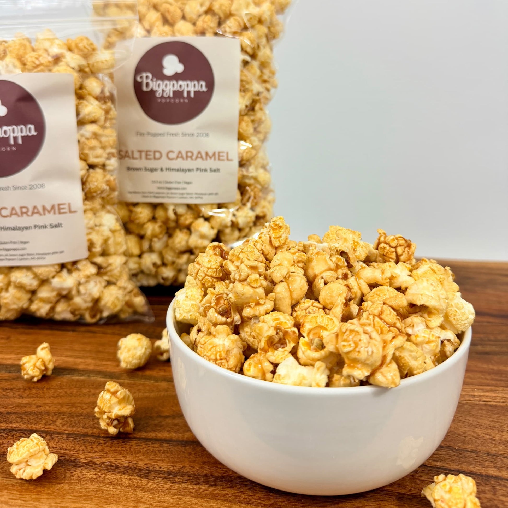 Bowl of Salted Caramel popcorn with a bag of popcorn in the background on a wooden surface.