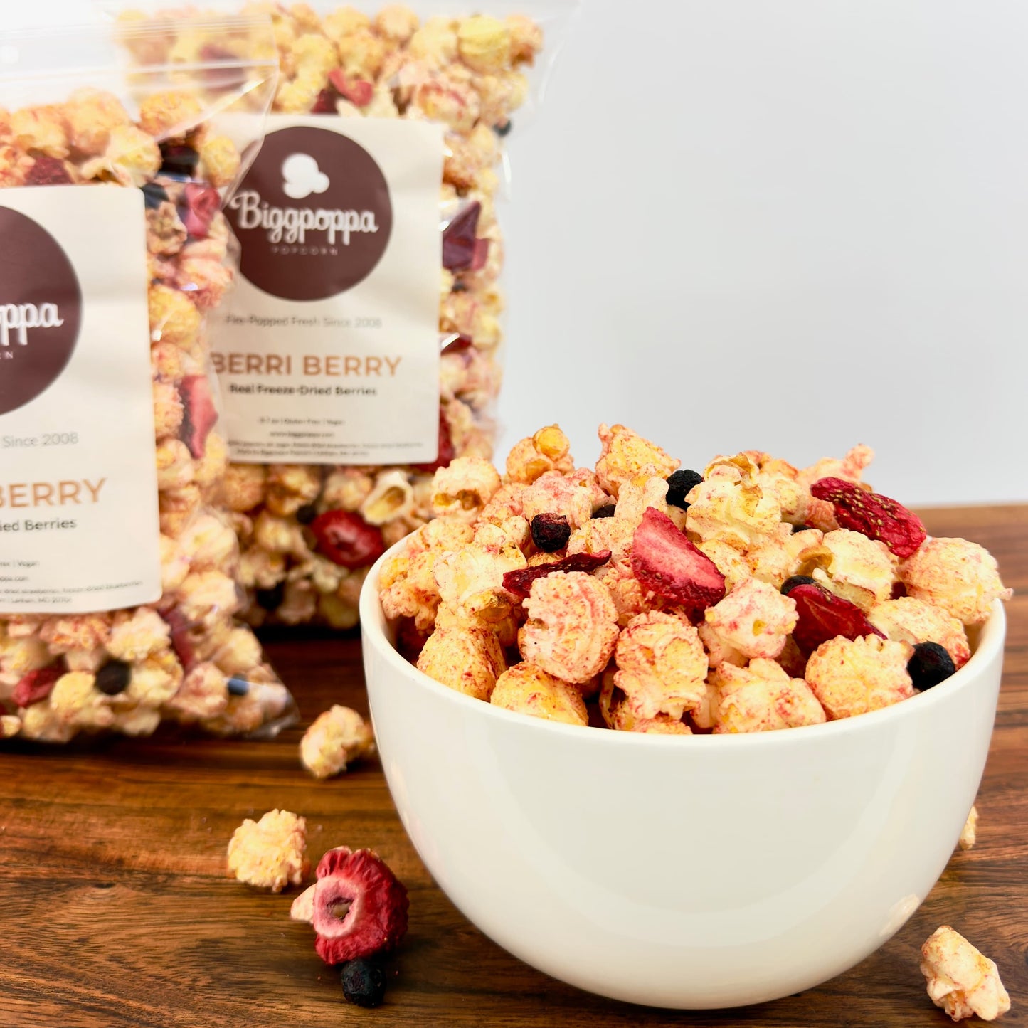 Bowl of popcorn with berries next to a bag of Biggopapa Berri Berry popcorn on a wooden surface.