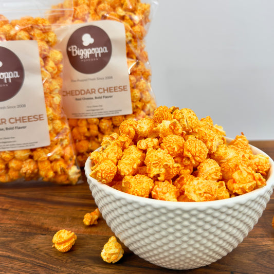 Bag of Cheddar Cheese popcorn with a bowl of popcorn on a wooden surface