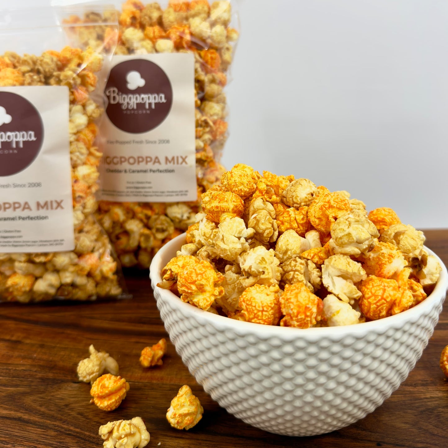 Bowl of popcorn with a bag labeled 'Biggpoppa Mix' on a wooden surface.